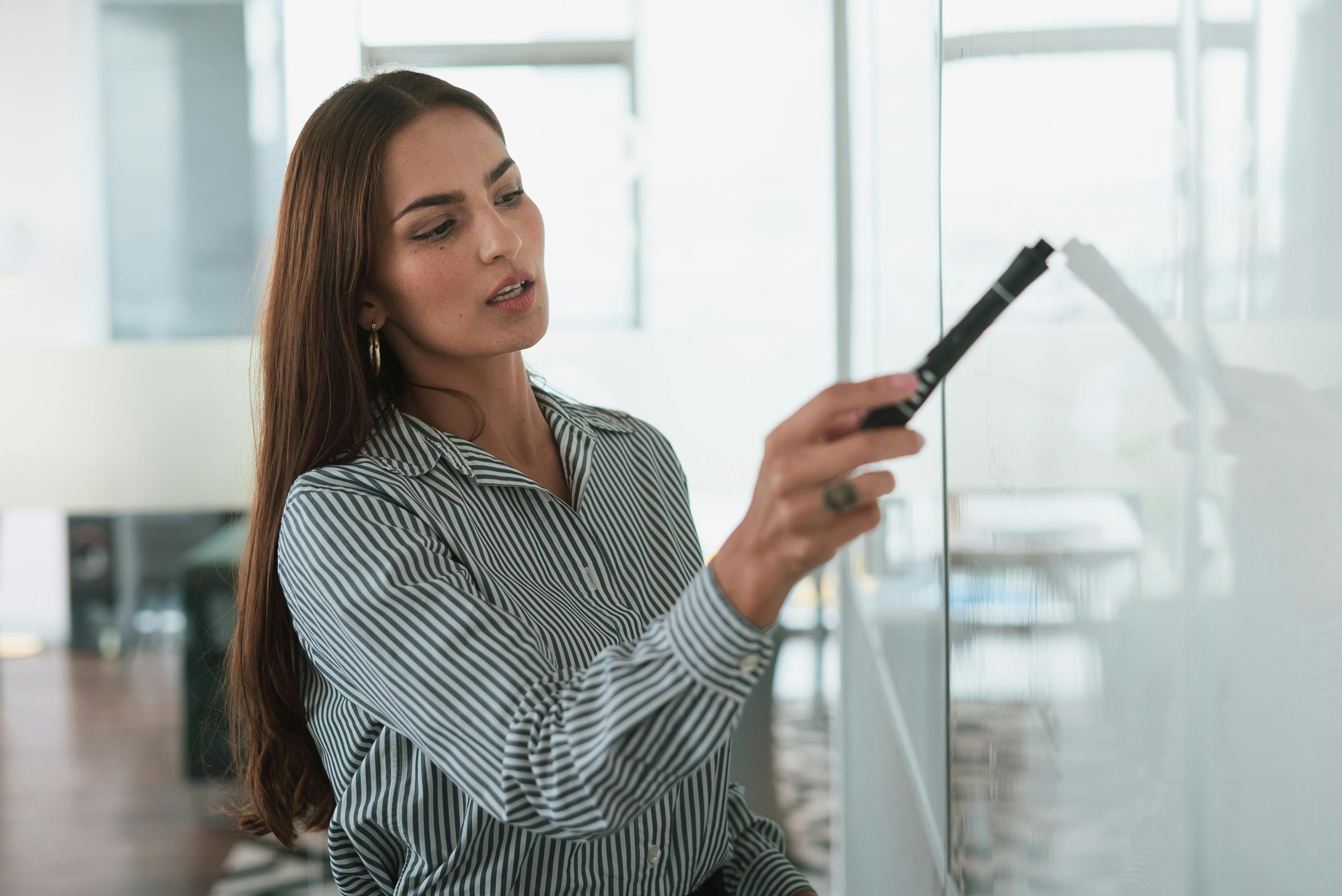 A focused businesswoman writing on a whiteboard during a presentation in a modern office.